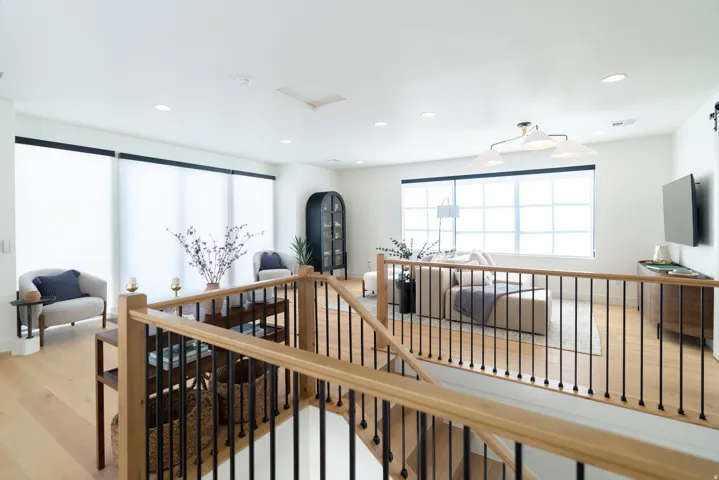 Hardwood flooring throughout, contemporary stair railing with wood-finish handrails and black balusters, recessed lighting, expansive windows with roller shades, and a modern chandelier