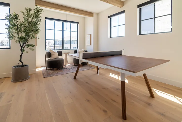 Light wood-finish flooring, exposed wood ceiling beams, white walls, and large black-framed windows
