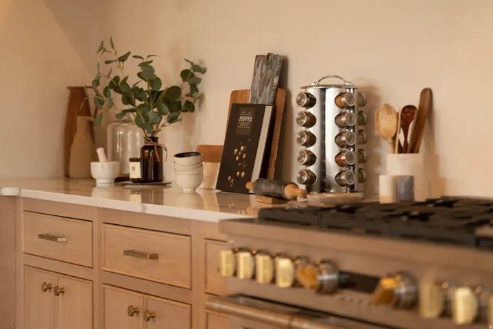 Chef's kitchen featuring stainless steel gas range with multiple burners, white quartz countertops, custom wood cabinetry with integrated hardware, and a rotating spice rack carousel