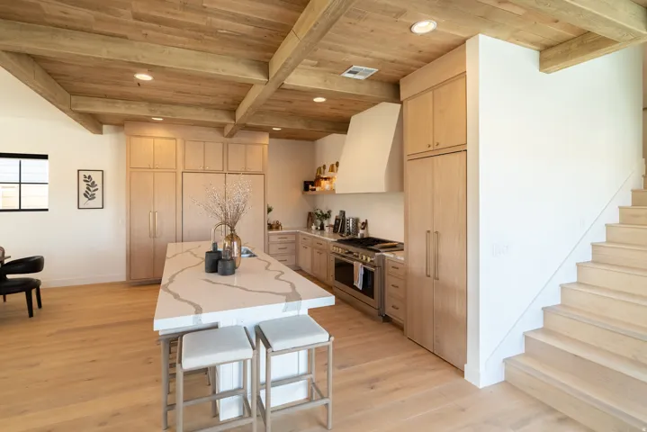 Kitchen featuring a large waterfall island with seating, integrated appliances, wood-finish flooring, and a wood-beamed ceiling