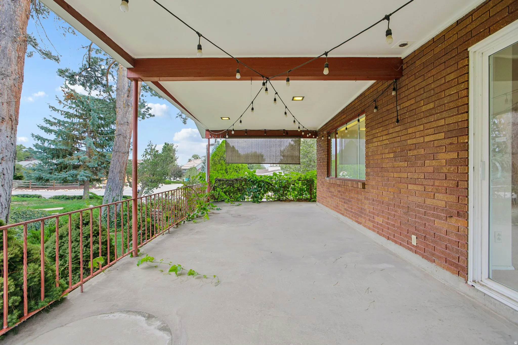 Expansive covered patio on south side of home featuring a concrete surface, metal railing, string lighting, and brick exterior wall