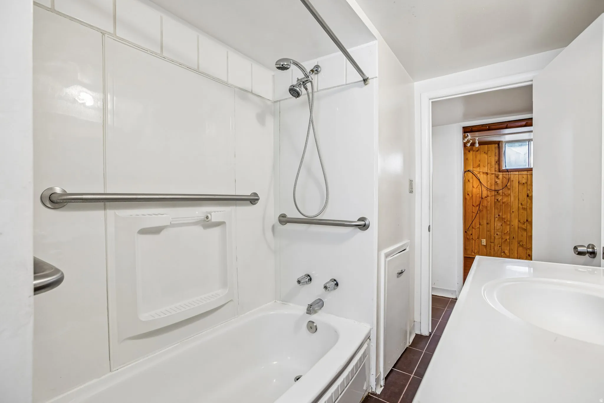 White bathtub with shower, brushed nickel fixtures, and grab bars