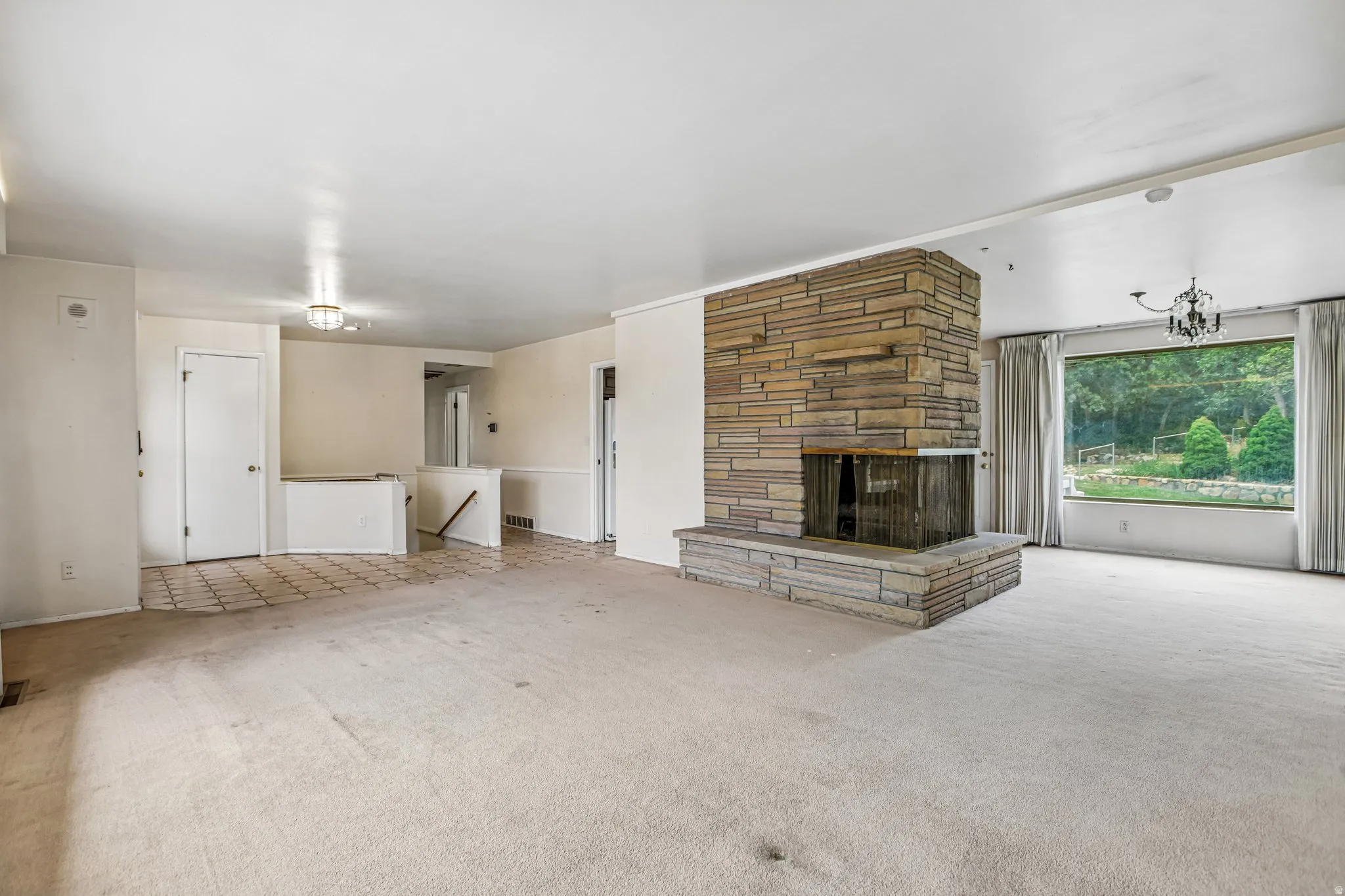 Stone-clad fireplace with hearth, large picture window, and chandelier light fixture