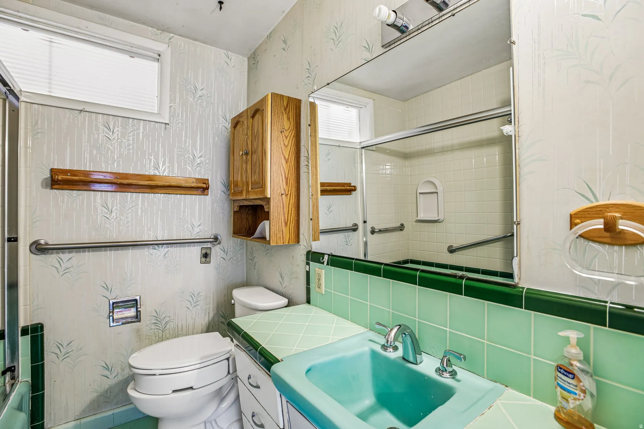 Bathroom featuring a ceramic tile countertop, integrated sink, large wall-mounted mirror, and overhead wood cabinetry