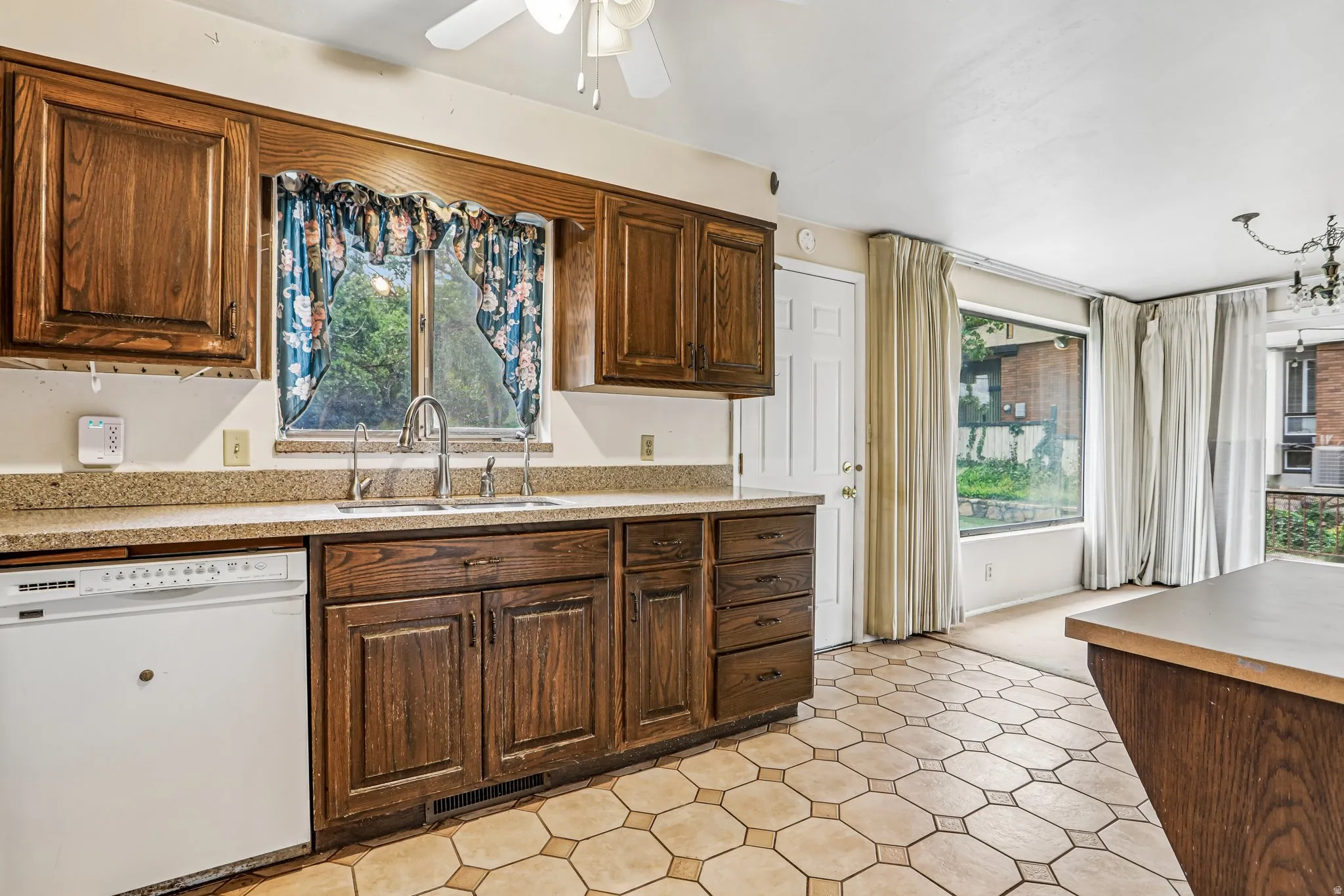 Kitchen featuring wood cabinetry, light-toned countertops, a stainless steel sink with a dual-handle faucet, and hexagonal floor tiling