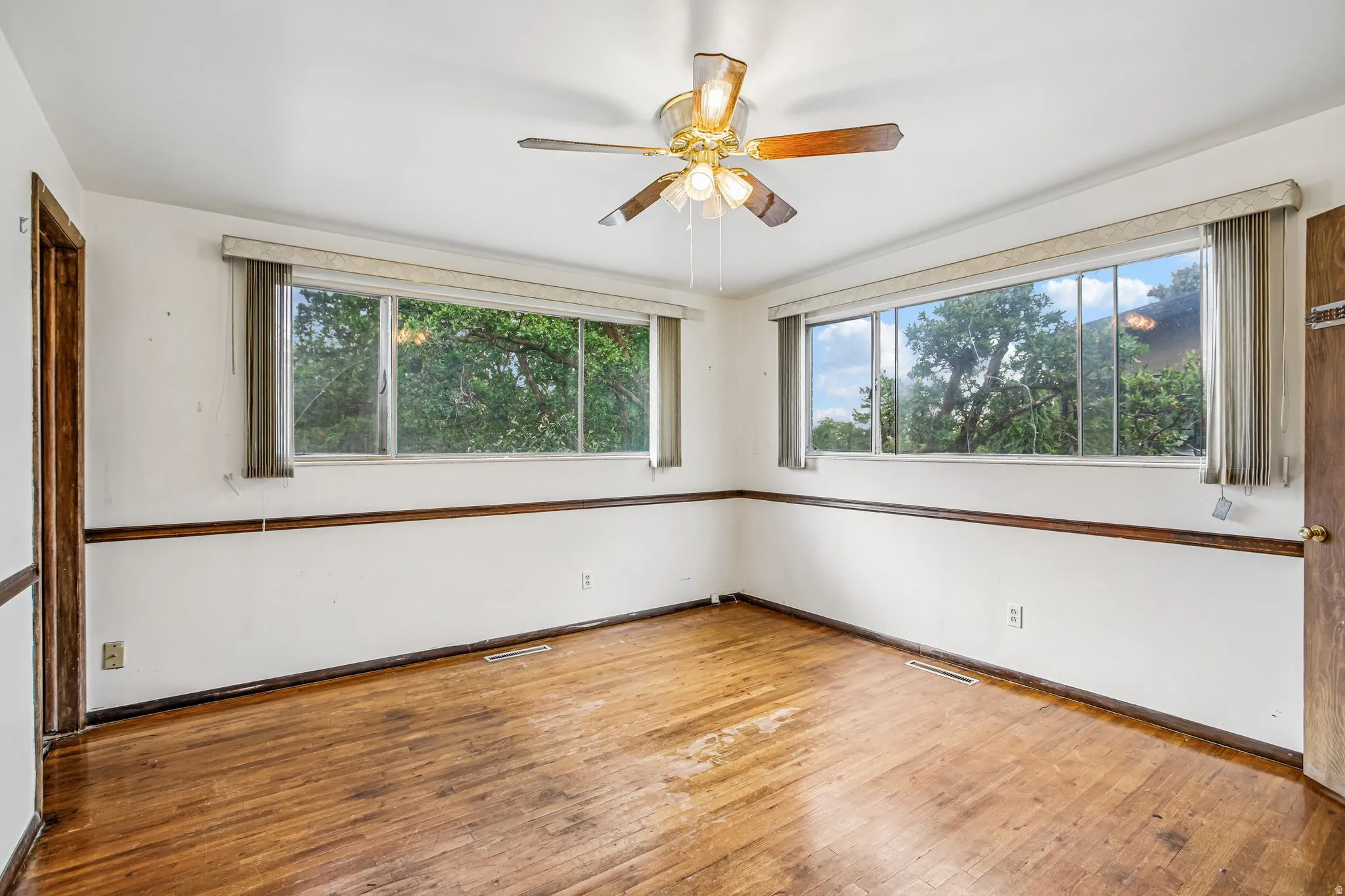 Hardwood flooring, two large windows, wood trim, and ceiling fan