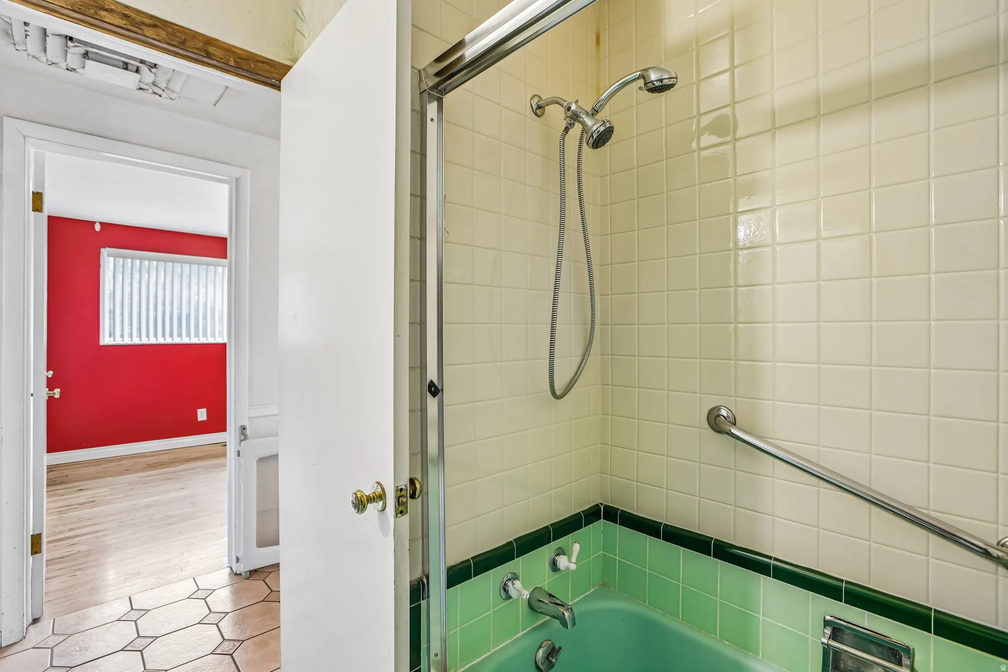 Green tiled bathtub with an integrated shower head and grab bar