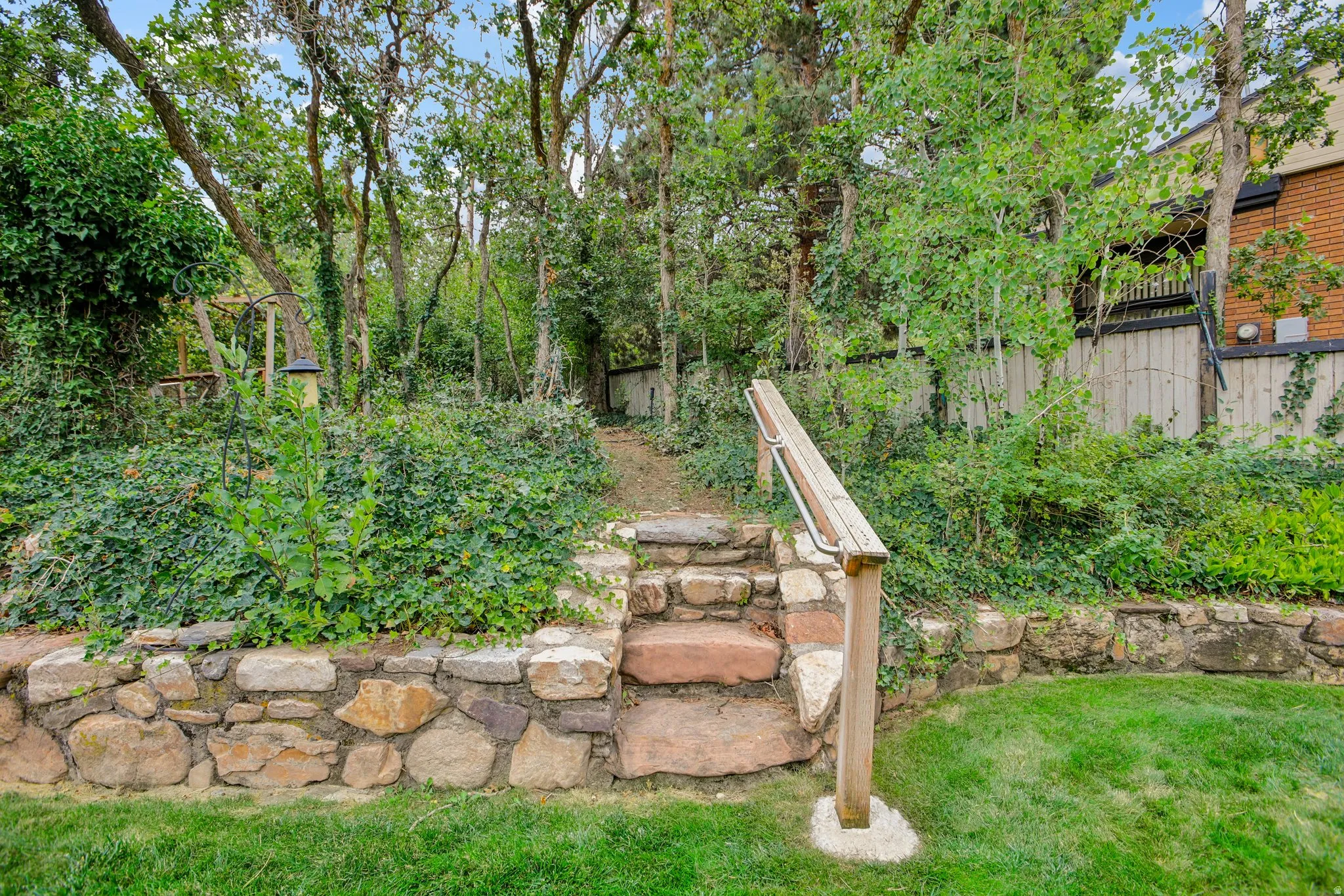 Stone retaining wall with integrated stone steps, wood handrail, and surrounding mature trees