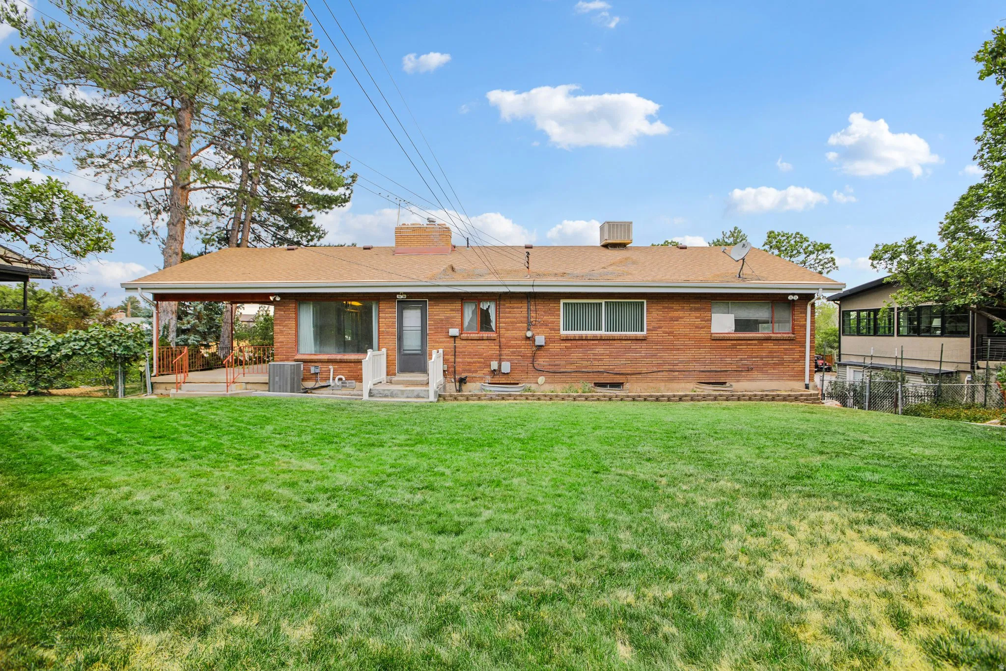 Expansive backyard featuring a brick exterior, covered patio, and mature trees