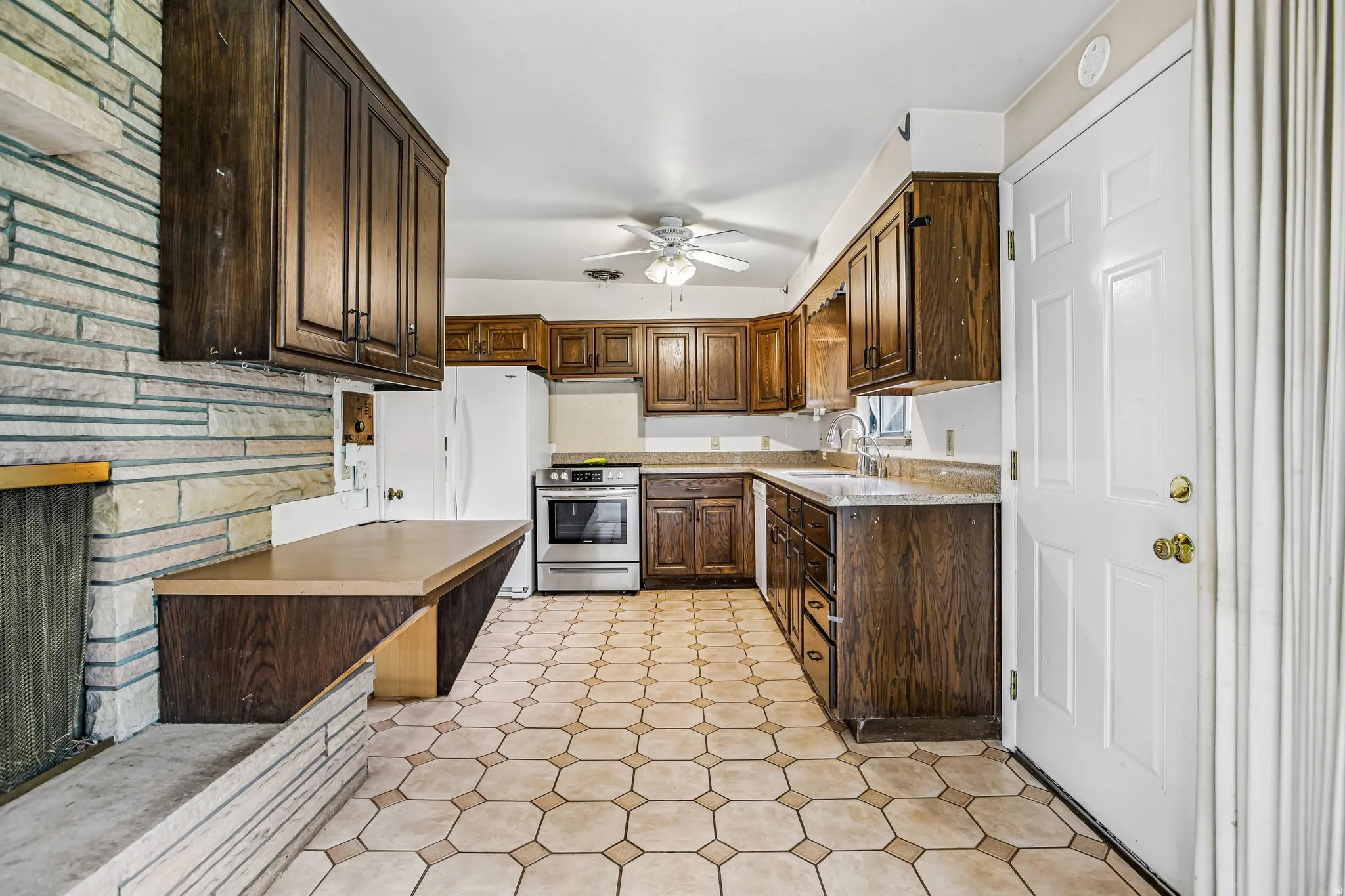 Kitchen featuring wood-finish cabinetry, tile flooring, stone-finish countertops, and a white ceiling fan
