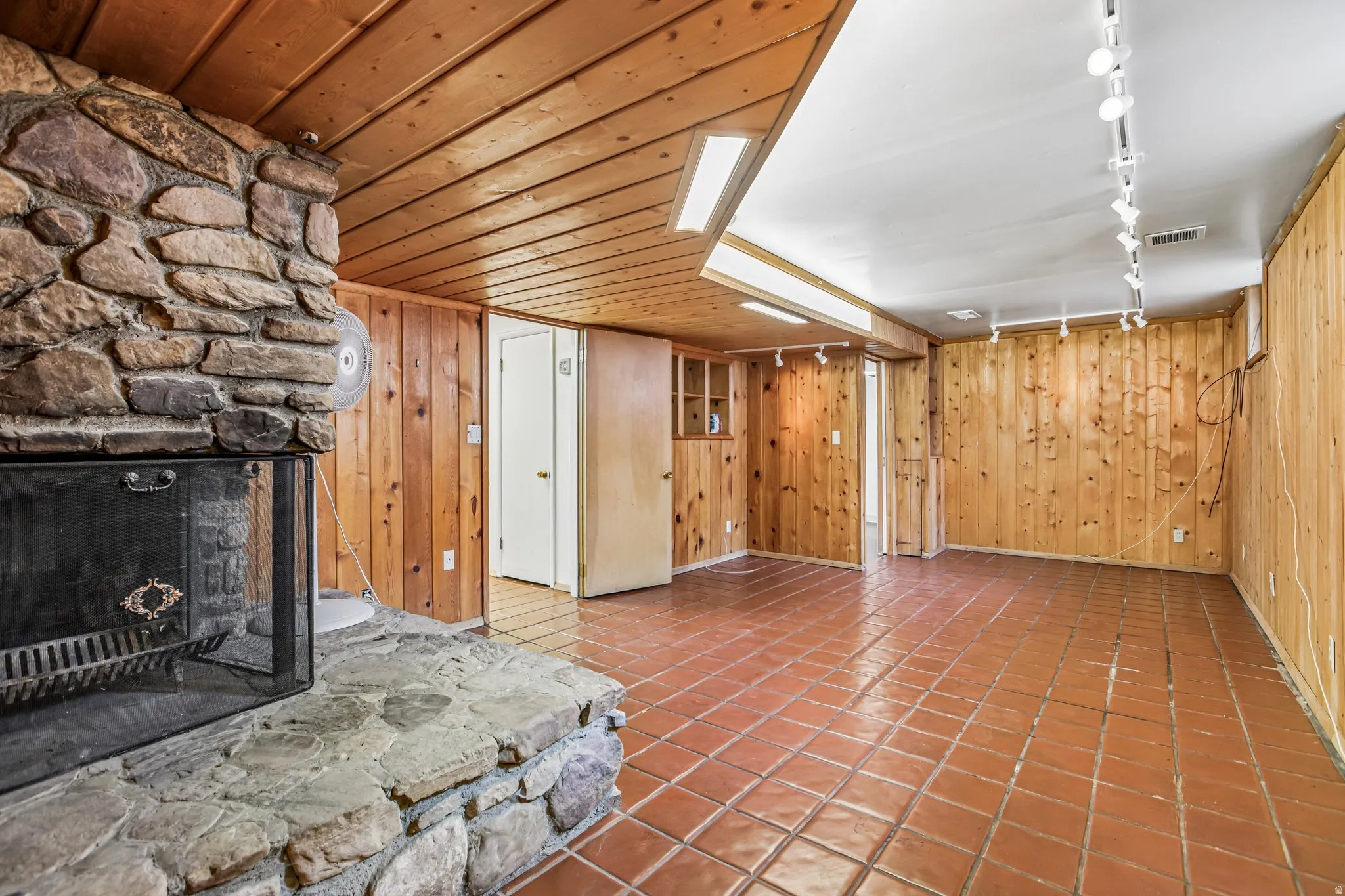 Stone fireplace with hearth, wood paneling, wood plank ceiling, terracotta tile flooring, track lighting fixtures