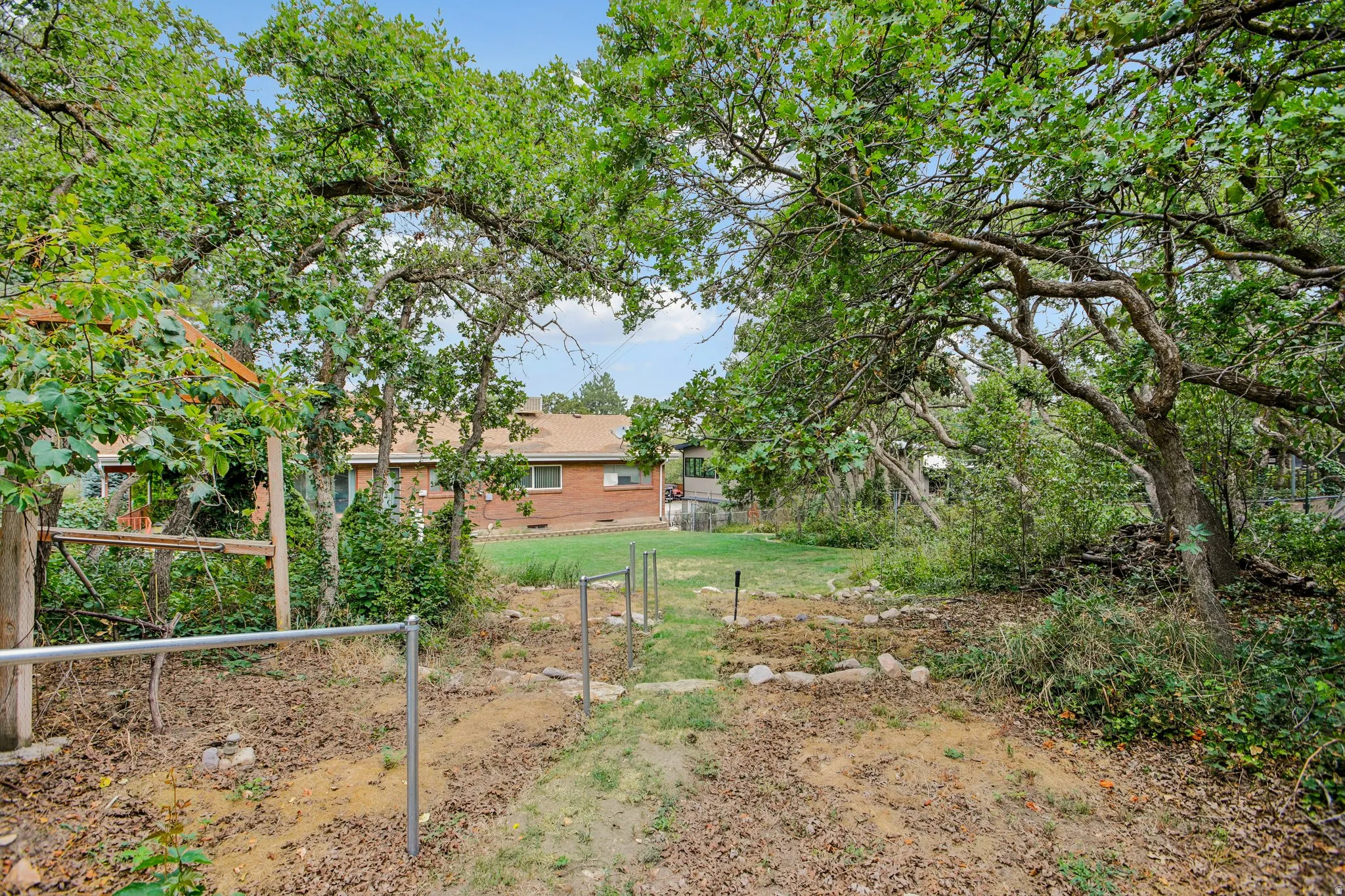Expansive yard featuring mature trees, a partial metal railing, and partial fencing
