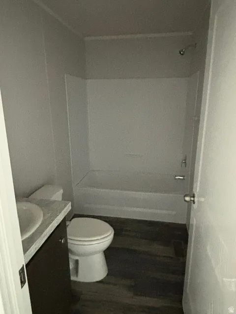 Wood-finish flooring, white bathtub with shower, white toilet, vanity with integrated sink, and a light-colored countertop