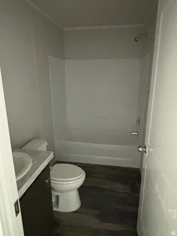 Wood-finish flooring, white bathtub with shower, white toilet, vanity with integrated sink, and a light-colored countertop
