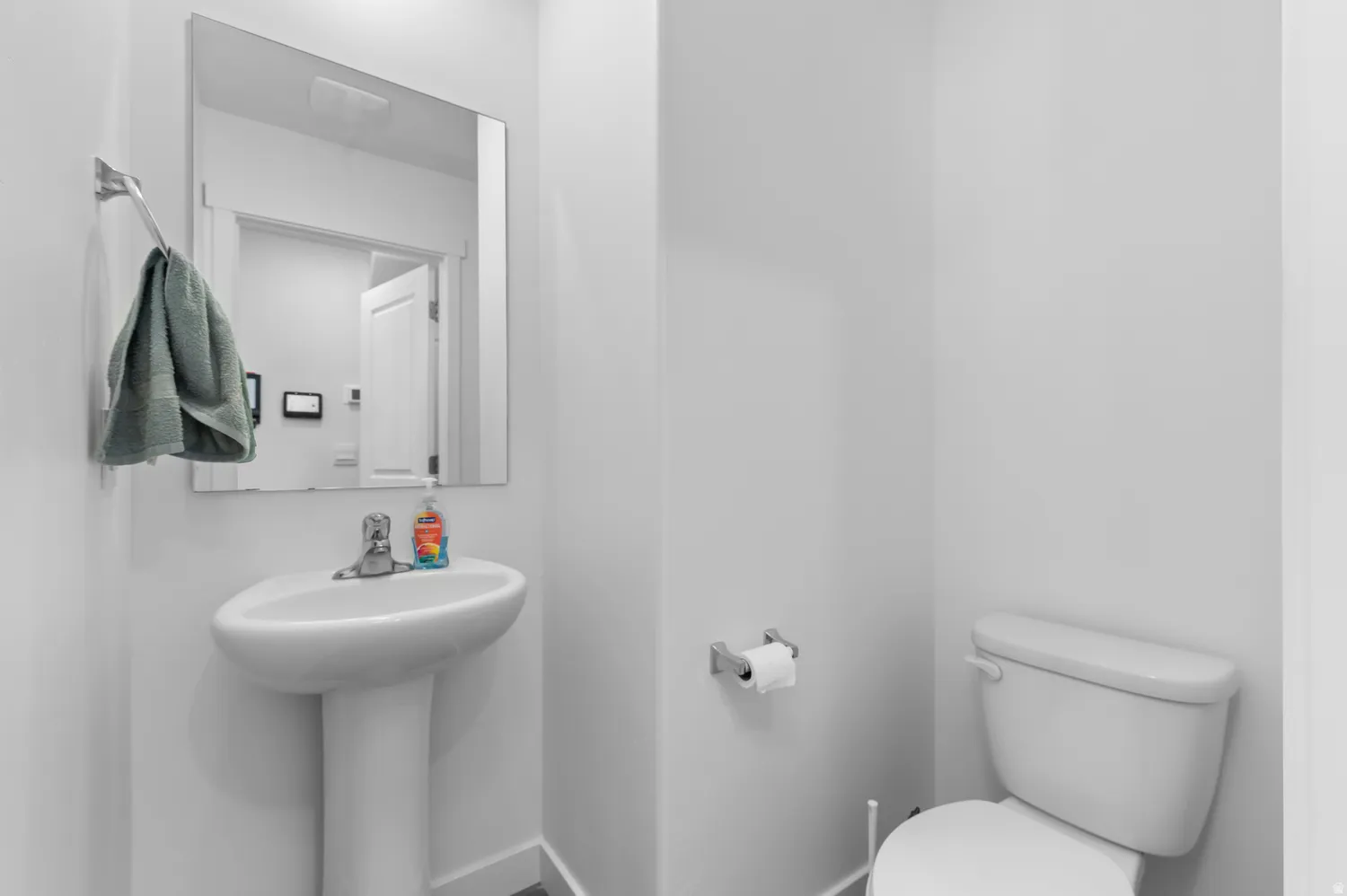 Pedestal sink with a polished chrome faucet, rectangular wall mirror, and modern white toilet