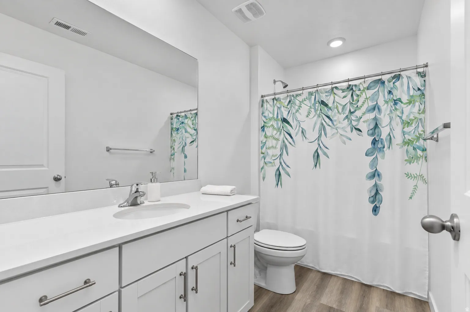 Bathroom featuring a single vanity with an integrated sink, white countertop, white cabinetry with silver hardware, and wood-finish flooring