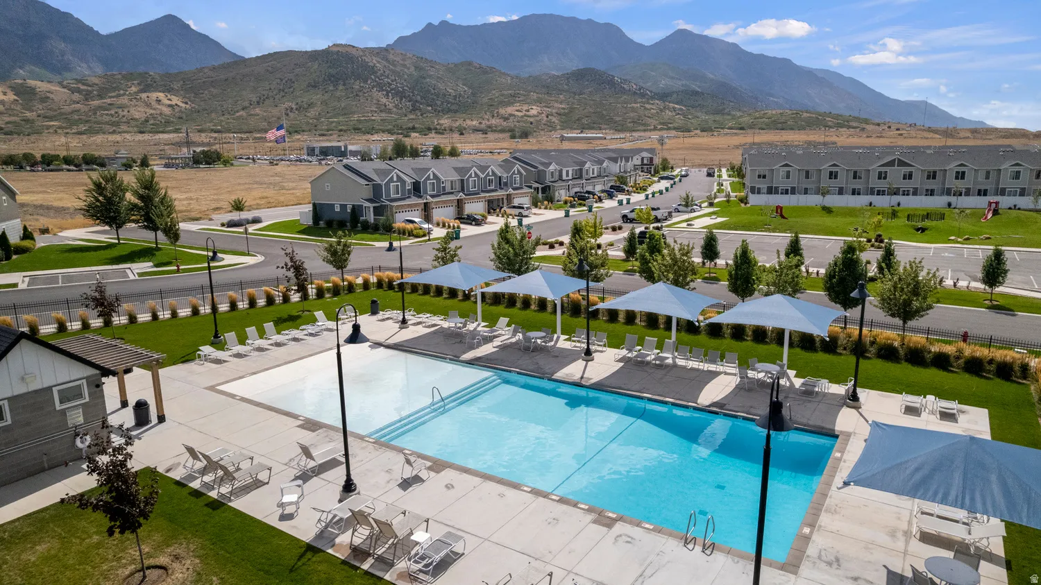 Community swimming pool with an adjacent spa, shaded lounging areas, and a nearby recreational building