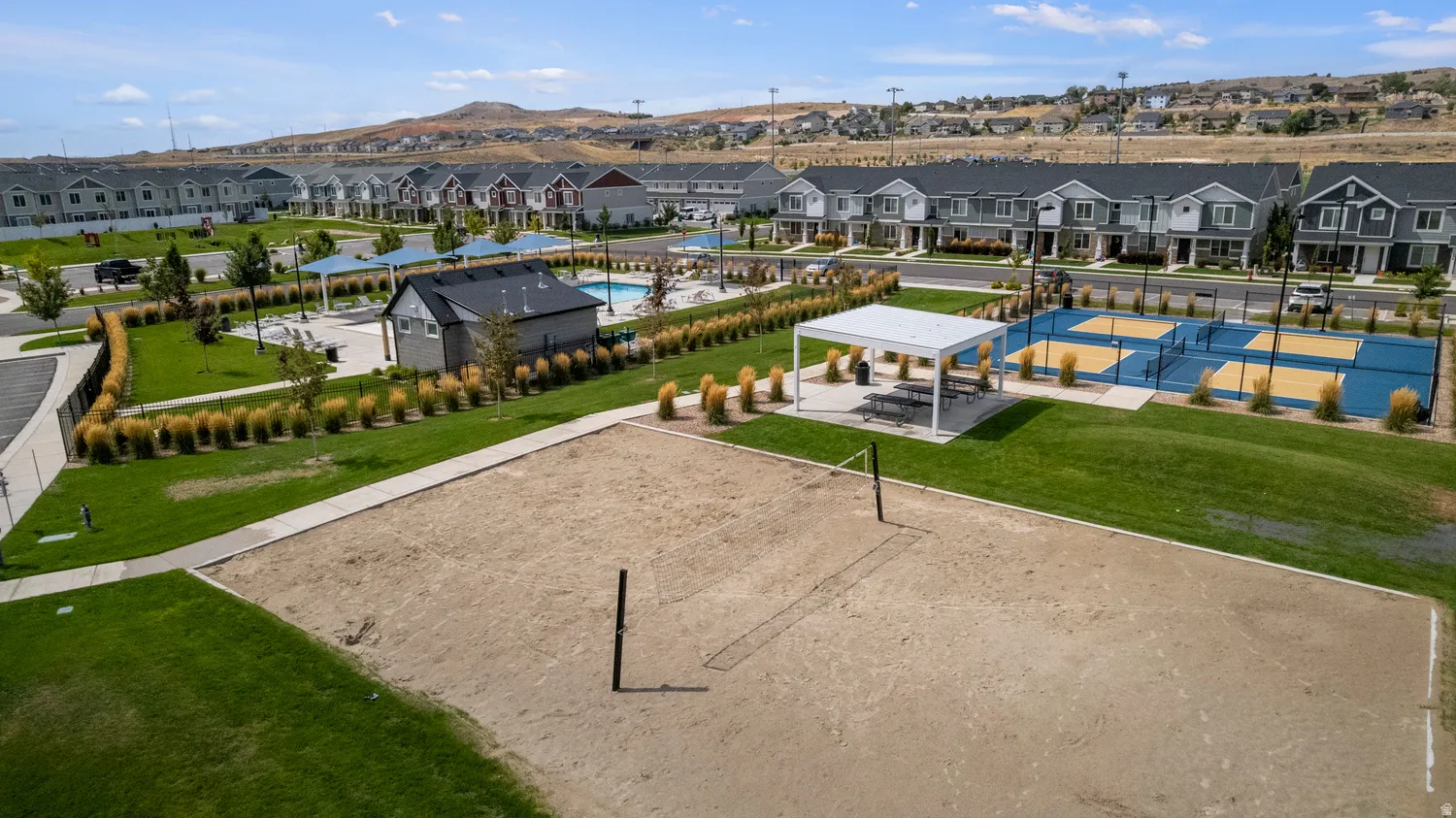 Sand volleyball court with a net, Pickleball courts, Swimming Pool bordered by green space and a concrete pathway