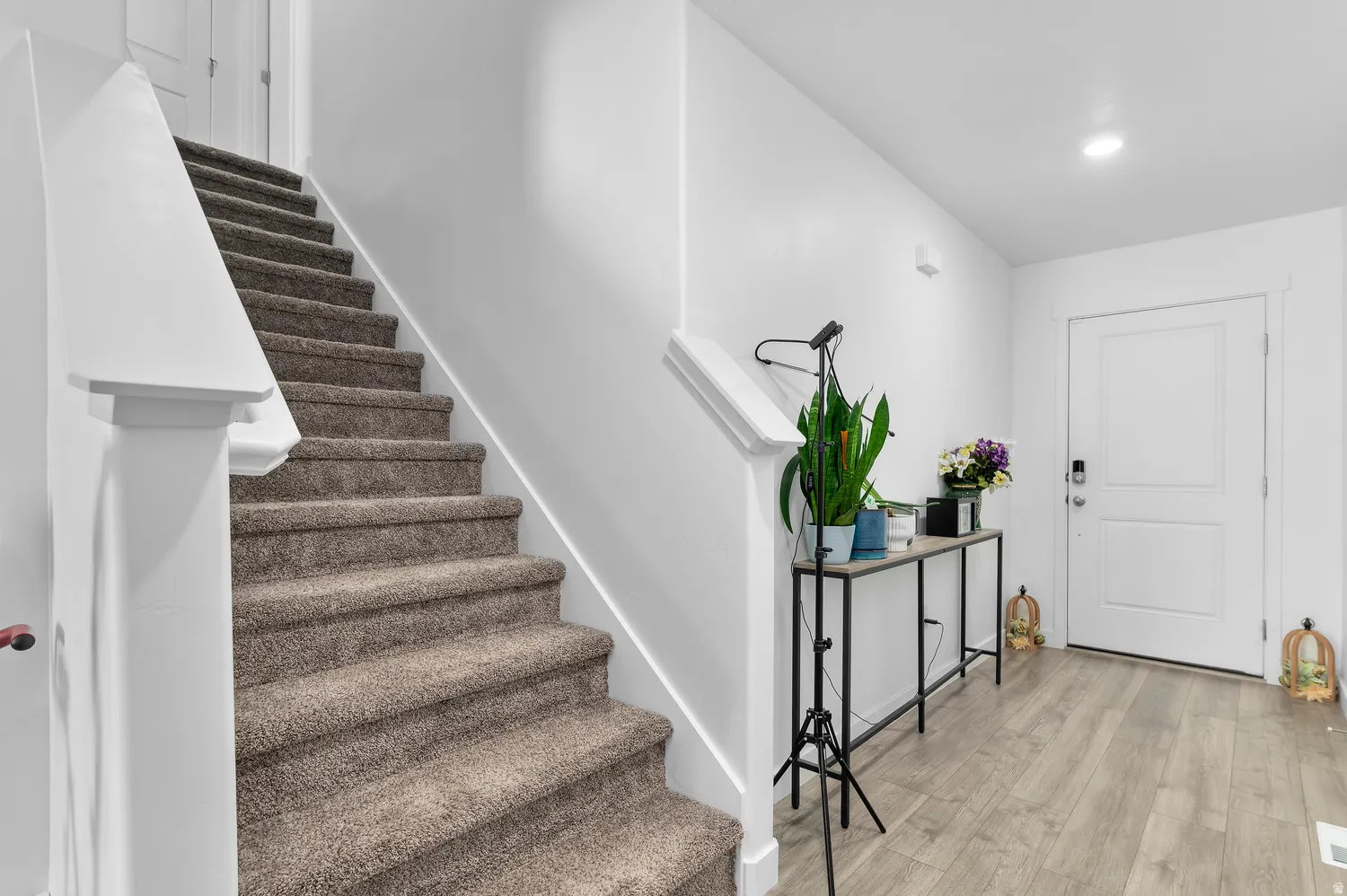 Carpeted staircase with white balustrade, wood-finish flooring, white paneled door, and recessed lighting