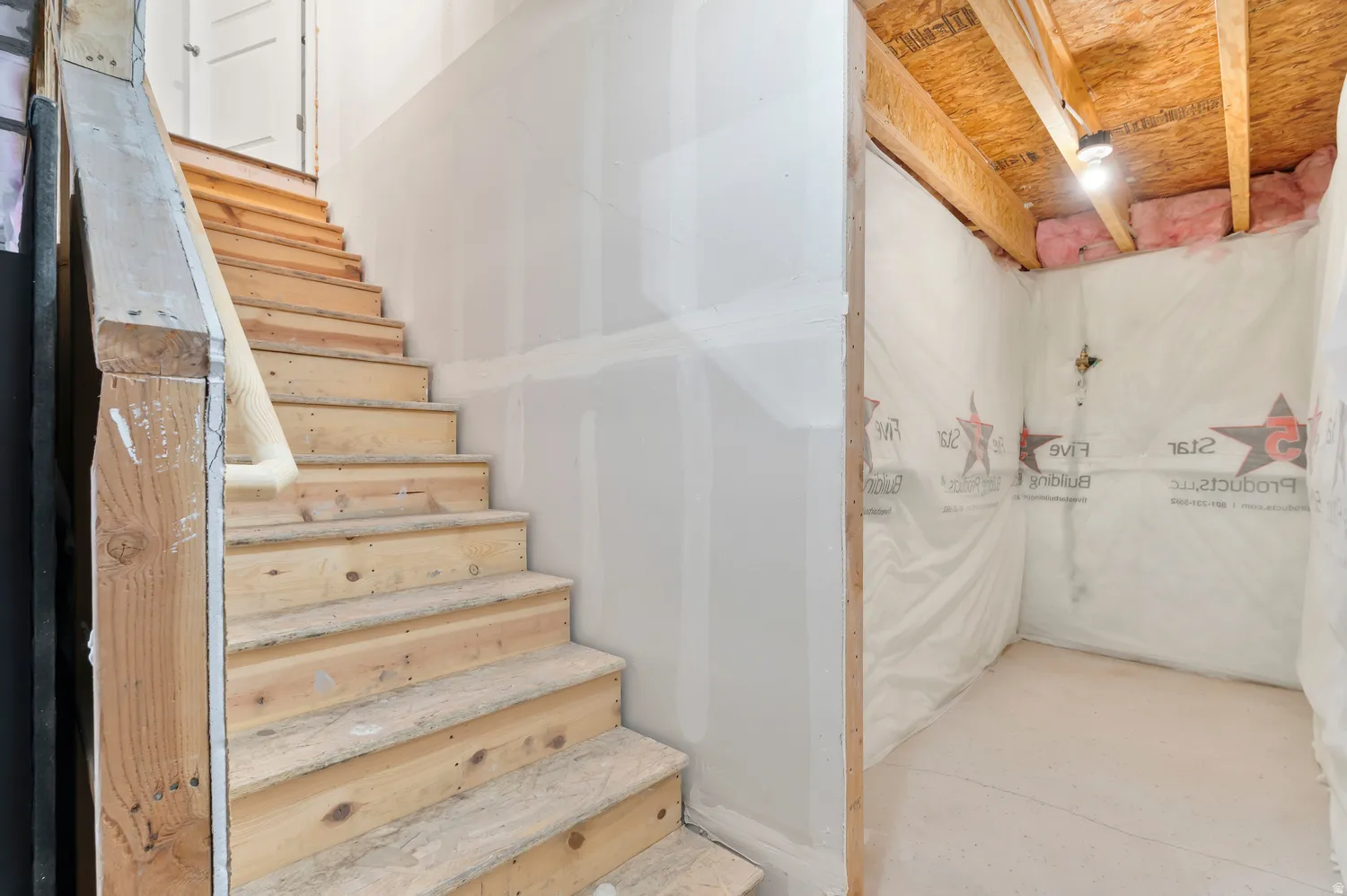 Unfinished wooden staircase with drywall on one side, and an unfinished storage area with exposed wood framing and insulation