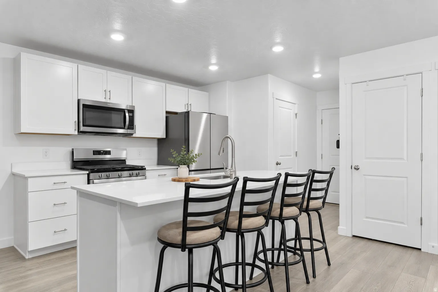 Kitchen featuring white cabinetry, stainless steel appliances, a center island with sink, recessed lighting, and wood-finish flooring