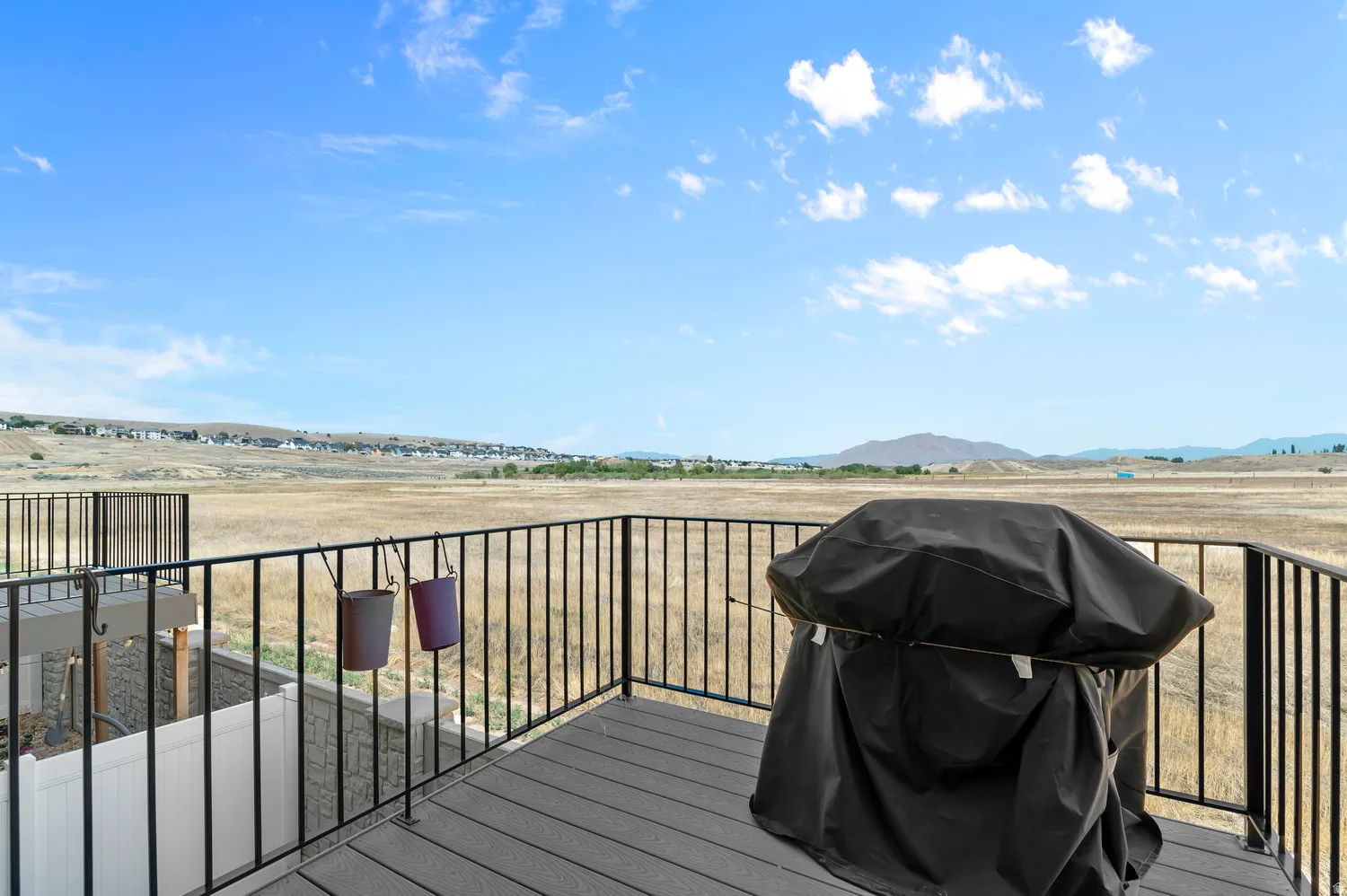 Expansive composite deck with metal railings overlooking open prairie landscape, featuring built-in grill with weather-protective cover and multiple storage solutions