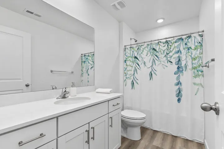 Bathroom featuring a single vanity with an integrated sink, white countertop, white cabinetry with silver hardware, and wood-finish flooring