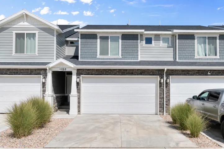 Two-story townhouse featuring stone and siding exterior, two attached garages, a covered entryway, and concrete driveways