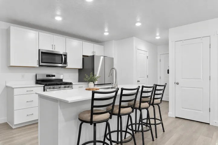 Kitchen featuring white cabinetry, stainless steel appliances, a center island with sink, recessed lighting, and wood-finish flooring