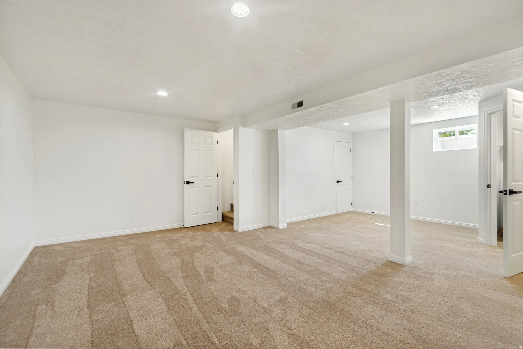 Expansive carpeted room with recessed lighting, white walls, and multiple paneled doors with dark hardware