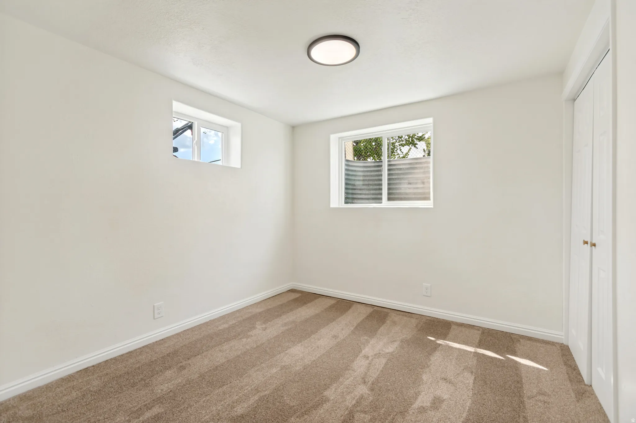 Plush carpet flooring, bright white walls, flush-mount ceiling light fixture, two windows, and bi-fold closet doors