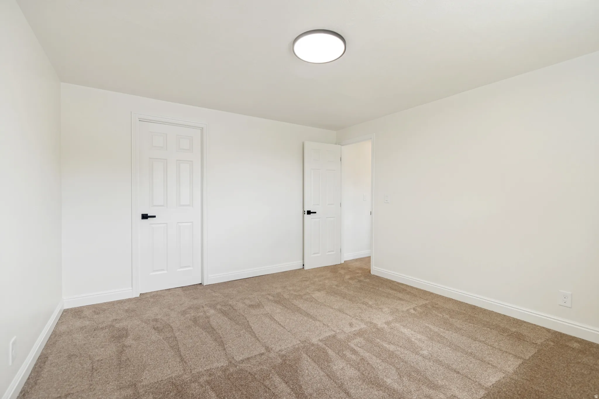 Spacious room featuring carpet flooring, white walls, and a modern flush-mount ceiling light