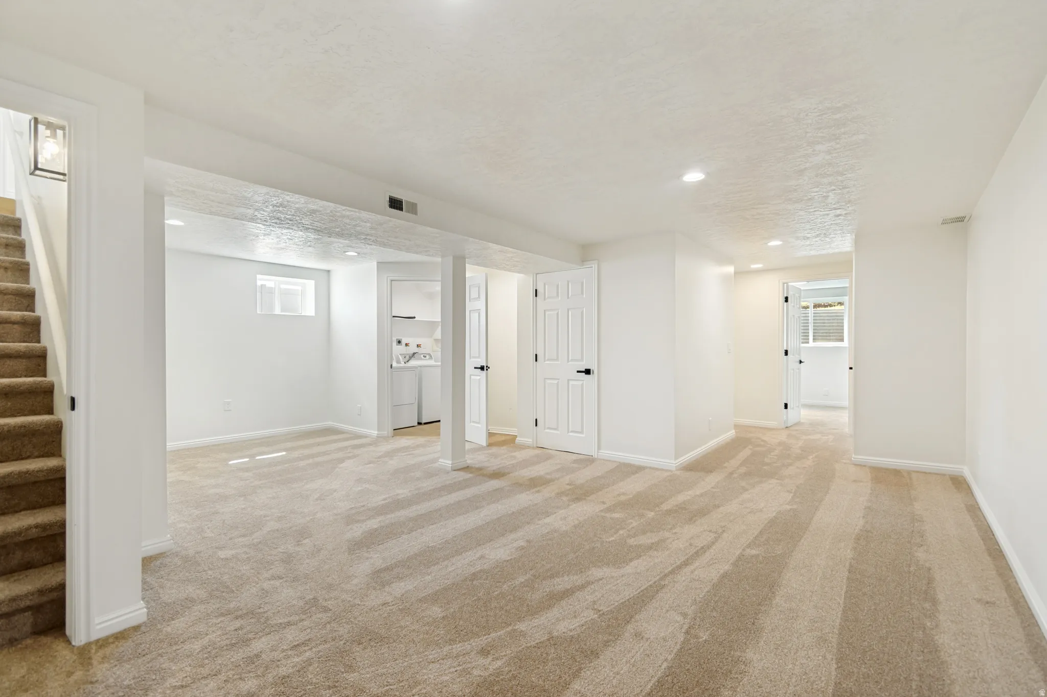 Neutral tone wall paint, light-colored carpet, recessed ceiling lighting, white interior doors, and a small built-in laundry area
