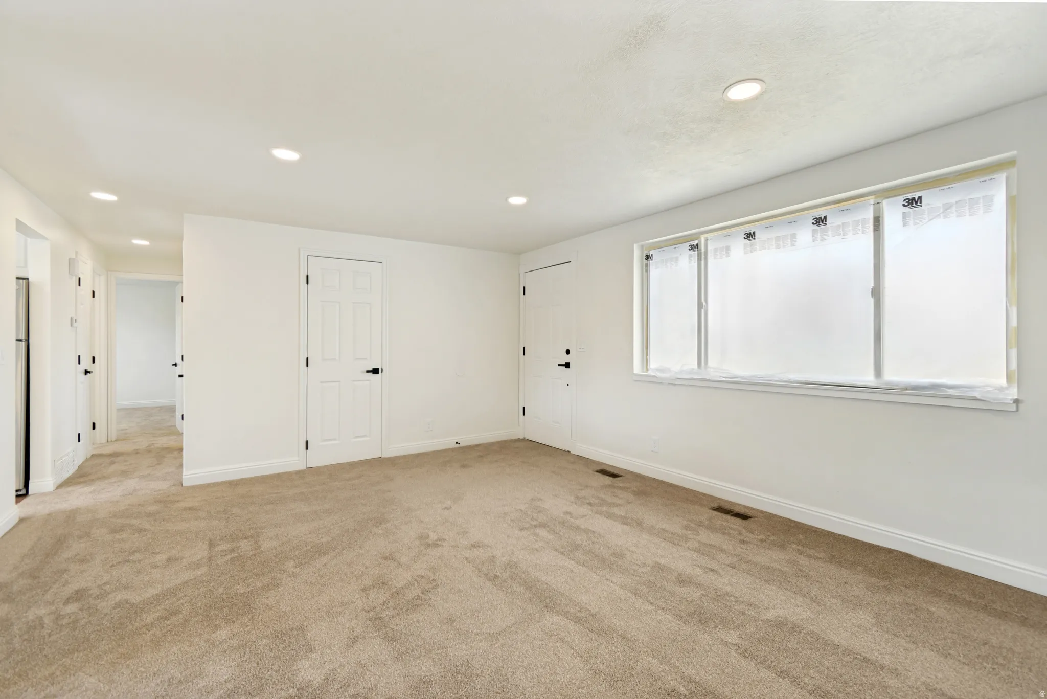 Recessed lighting, light beige carpeting, white walls, white trim, and white paneled doors with black hardware