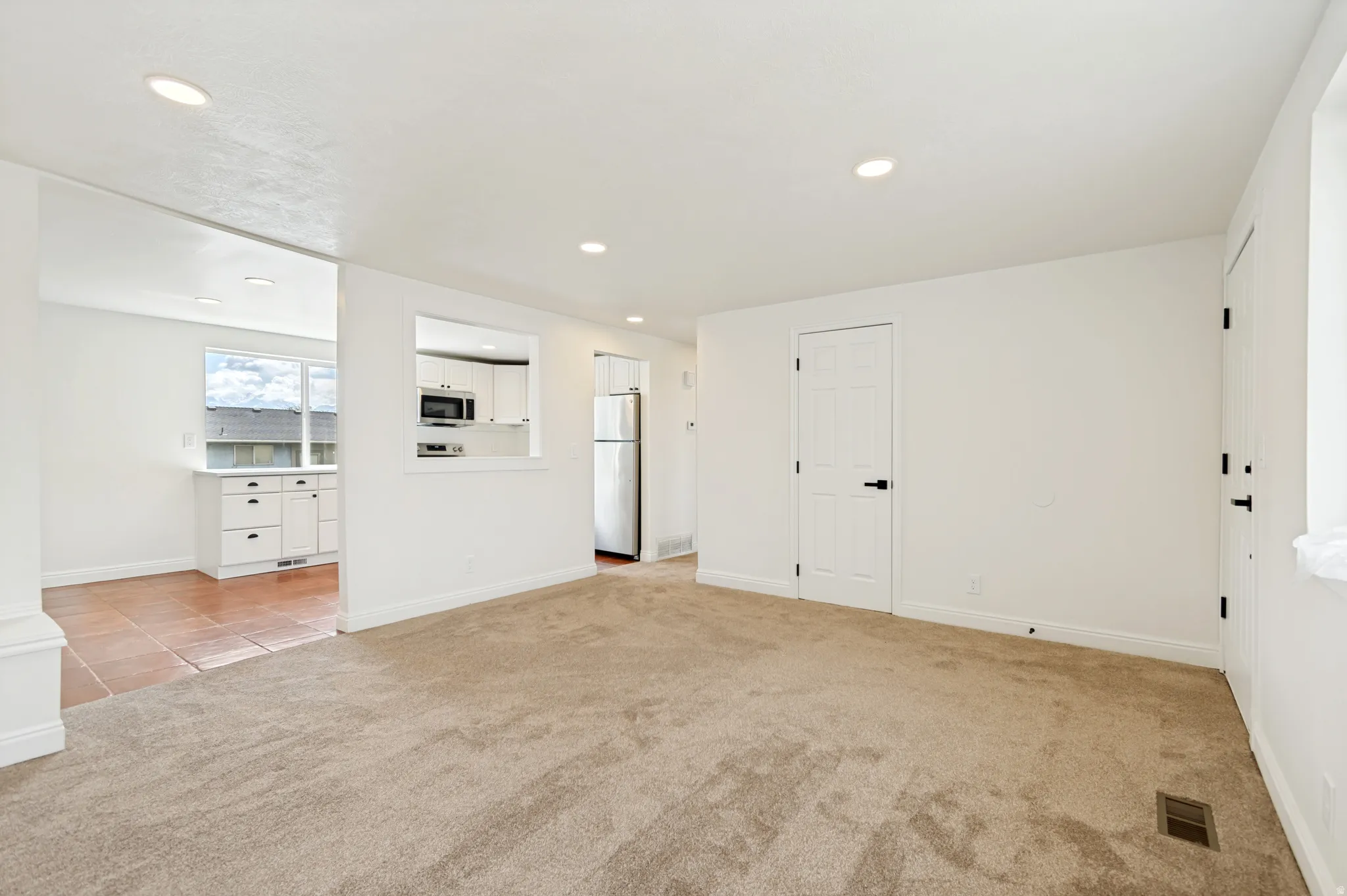 Recessed lighting, neutral carpeting, crisp white walls, and white paneled doors with matte black hardware