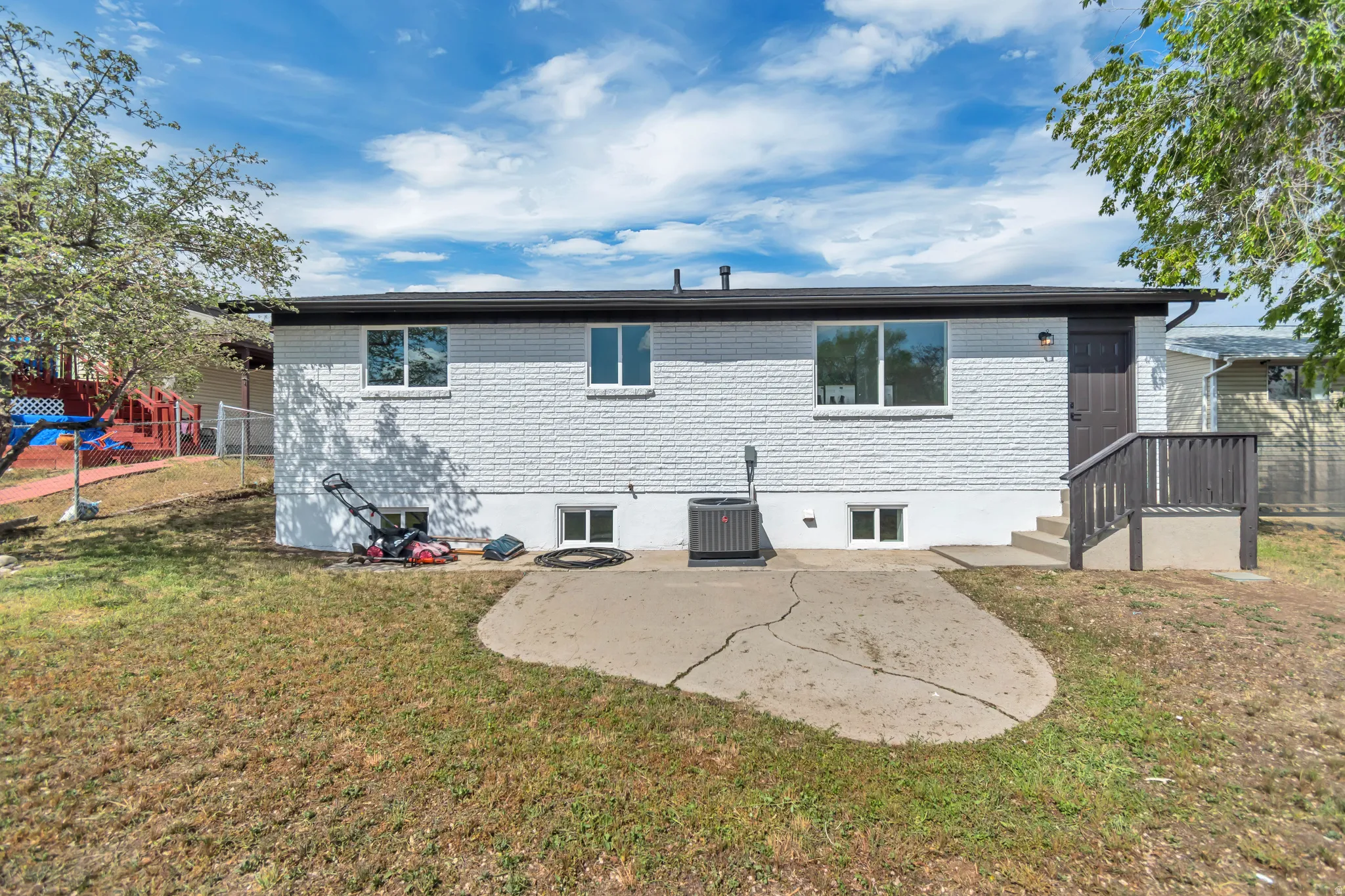 White brick exterior with a dark trim roofline, multiple windows, a concrete patio, and exterior stairs with a railing