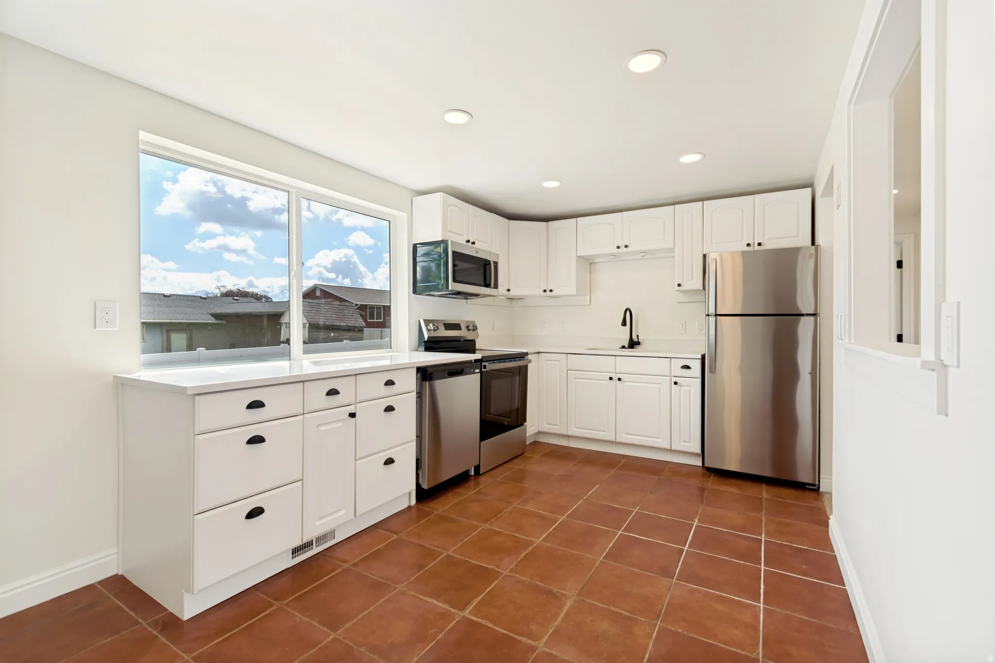 White cabinetry with matte black hardware, stainless steel appliances, white countertops, tile flooring, and recessed ceiling lighting