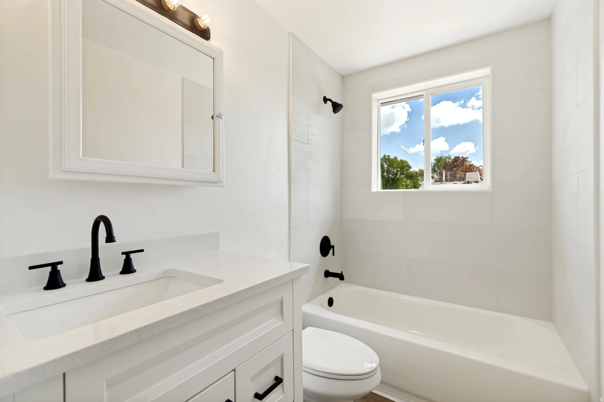 White vanity with integrated sink, black fixtures, and a framed mirror