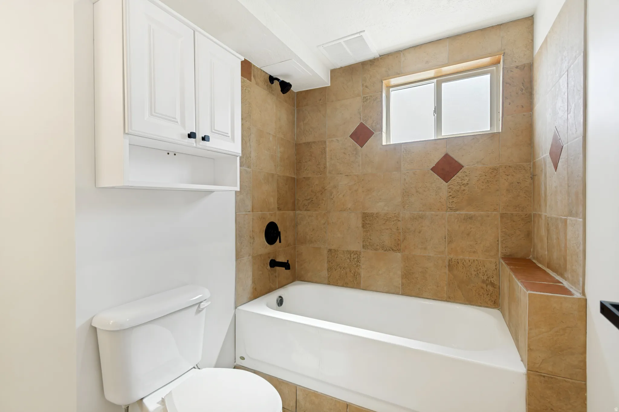 Wall-mounted white cabinetry with black hardware, tiled shower surround with accent tiles, built-in shower bench, white bathtub, and a window for natural light
