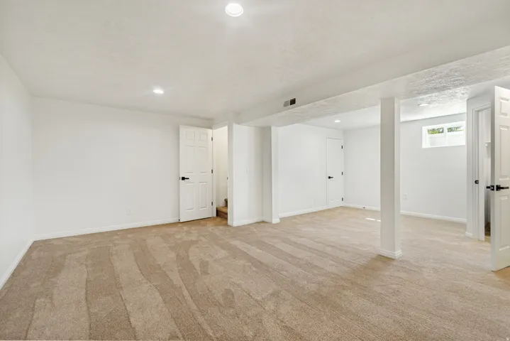Expansive carpeted room with recessed lighting, white walls, and multiple paneled doors with dark hardware
