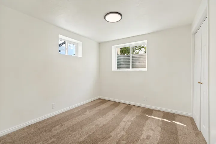 Plush carpet flooring, bright white walls, flush-mount ceiling light fixture, two windows, and bi-fold closet doors