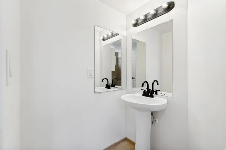 Pedestal sink with matte black faucet, wall-mounted mirror, and overhead vanity lighting
