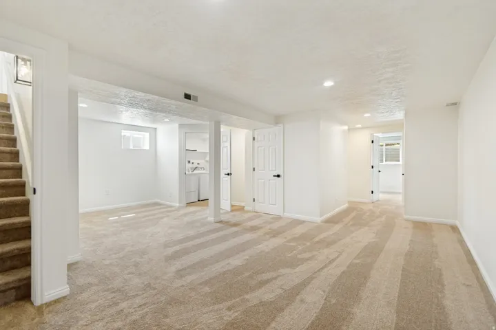 Neutral tone wall paint, light-colored carpet, recessed ceiling lighting, white interior doors, and a small built-in laundry area