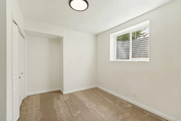 Neutral wall paint, carpeted flooring, window with exterior well, bi-fold closet doors, and a ceiling-mounted light fixture