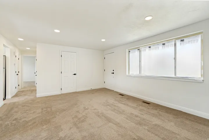 Recessed lighting, light beige carpeting, white walls, white trim, and white paneled doors with black hardware