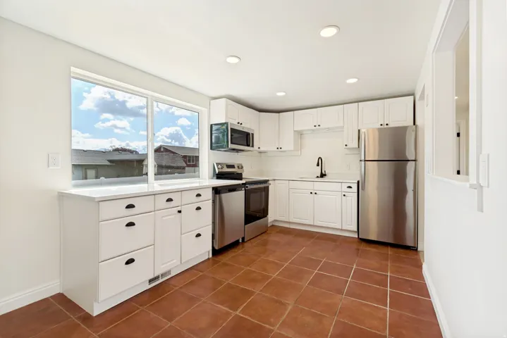 White cabinetry with matte black hardware, stainless steel appliances, white countertops, tile flooring, and recessed ceiling lighting