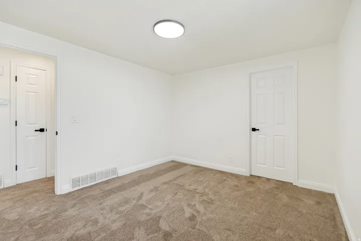 Light-colored carpeting, white walls, and a contemporary flush-mount ceiling light