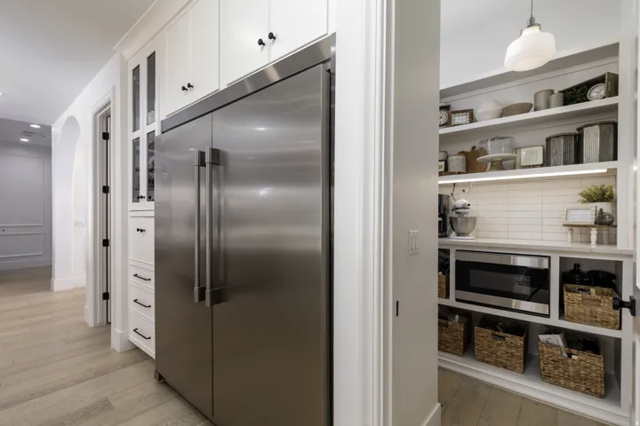 Stainless steel refrigerator, white shaker cabinetry with glass accents, wood-finish flooring, built-in pantry shelving, and subway tile backsplash