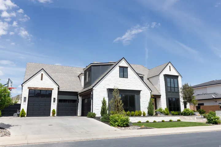 White brick exterior with dark trim accents, multi-pane windows, a pitched tile roof, and an attached two-car garage