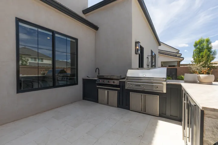 Outdoor kitchen featuring an integrated stainless steel grill, a built-in sink, dark cabinetry, and stone-finish countertops